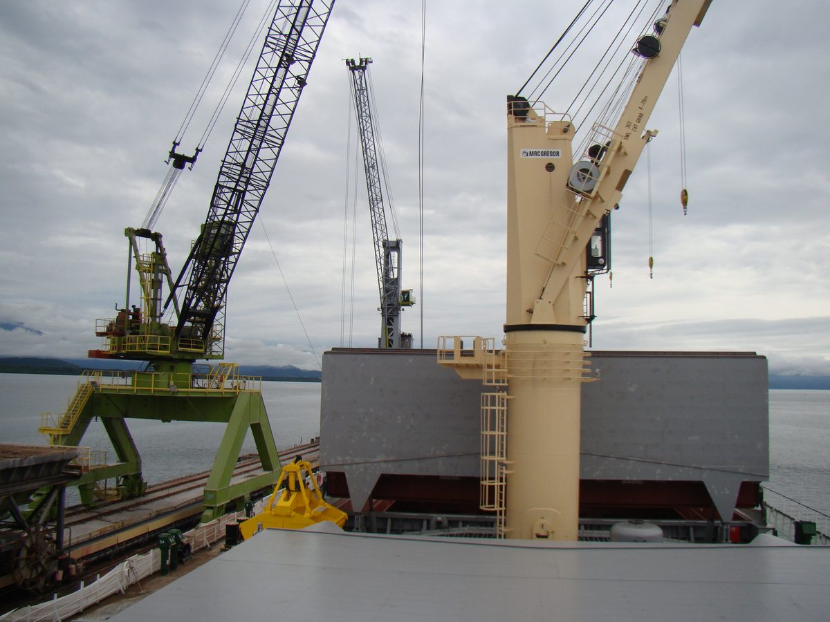 Guindastes de bordo e de terra posicionados sobre os porões de um navio graneleiro